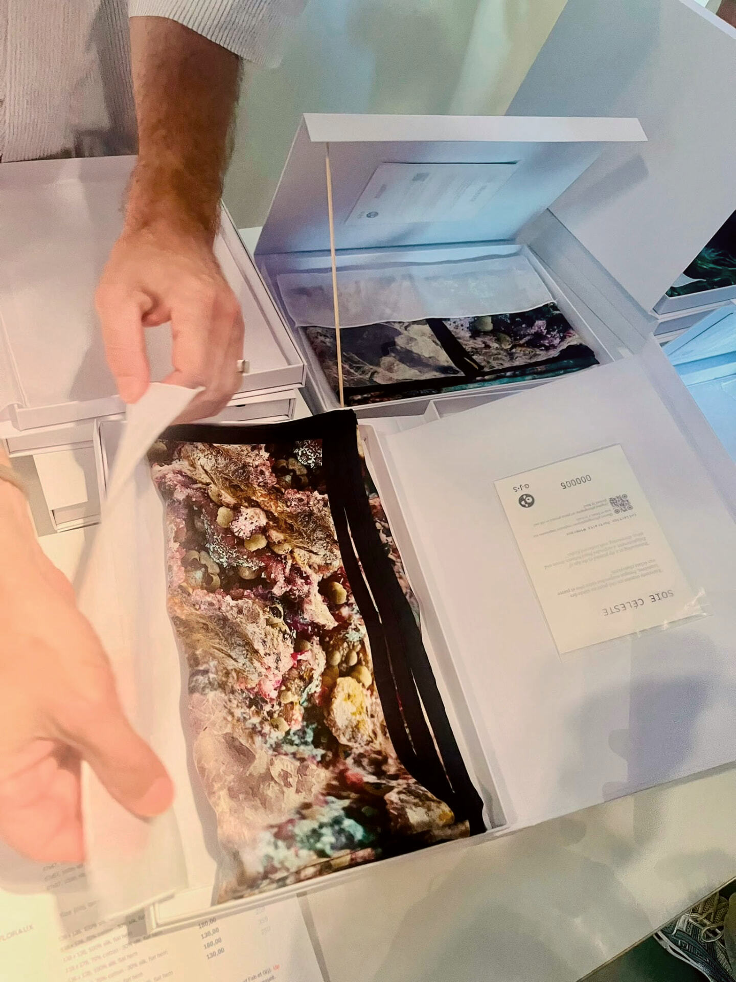 Carré de soie tenu au-dessus de son coffret d'édition ouvert